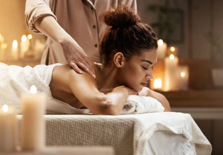 A guest resting on a spa bed with lit candles in the foreground while a therapist works on her back