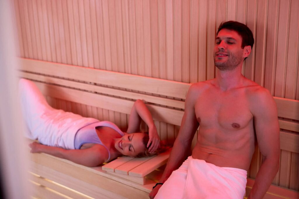A man and a woman relaxing with their eyes closed in a warm, wood-panelled sauna
